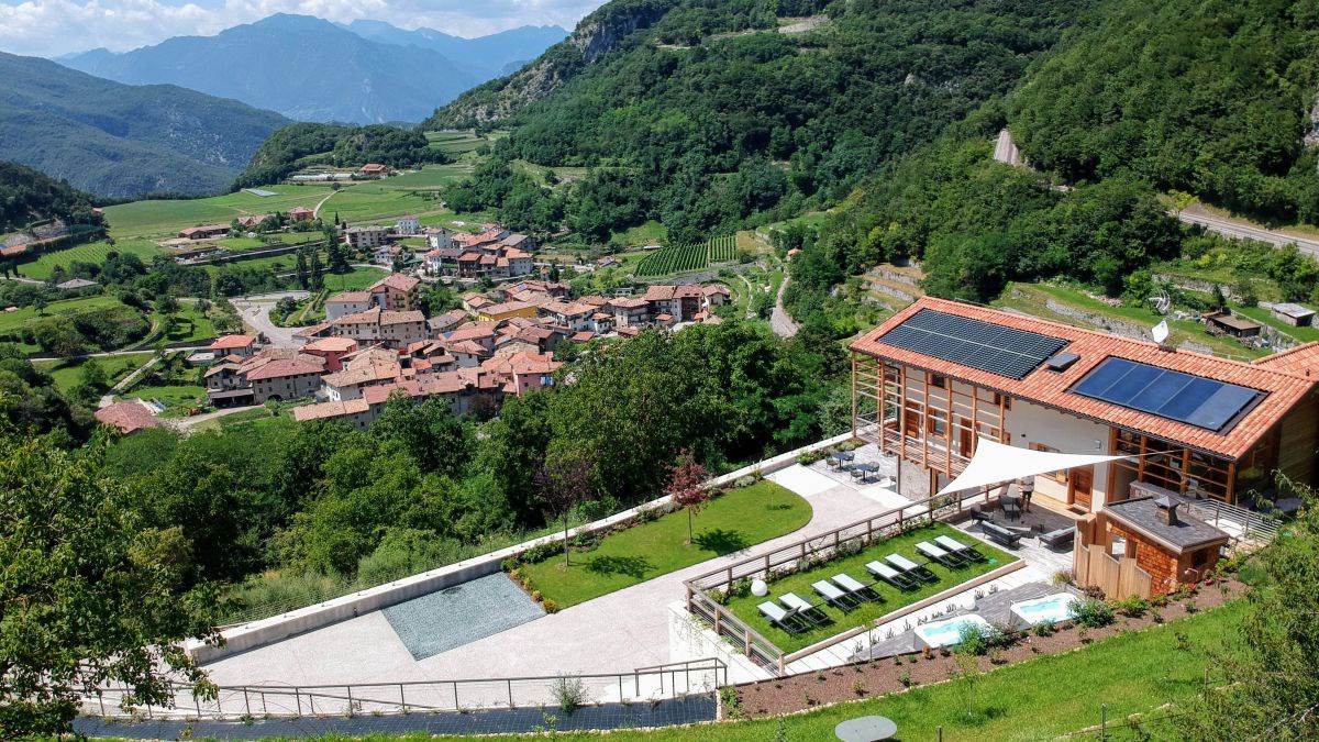 Aufnahme von oben. Man sieht das Haus mit Solarzellen am Dach, den Vorgarten mit Liehen und Whirlpools. Im Hintergrind ein kleiner Ort.