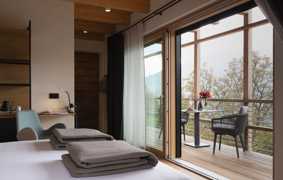 Blick vom Zimmer über das Doppelbett hinaus auf den Balkon und in die Landschaft.