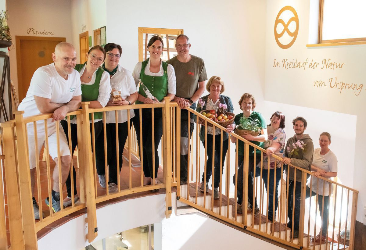 10 Personen stehen aufgefädelt auf einer Treppe und blicken über das Holzgeländer in die Kamera.