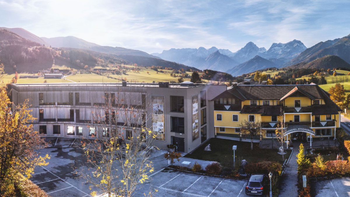 Aussenansicht im Sommer: Rechts der Altbau, links ein halbrunder Neibeu, im Hintergrund die Gebirgskette mit großem und kleinem Priel.