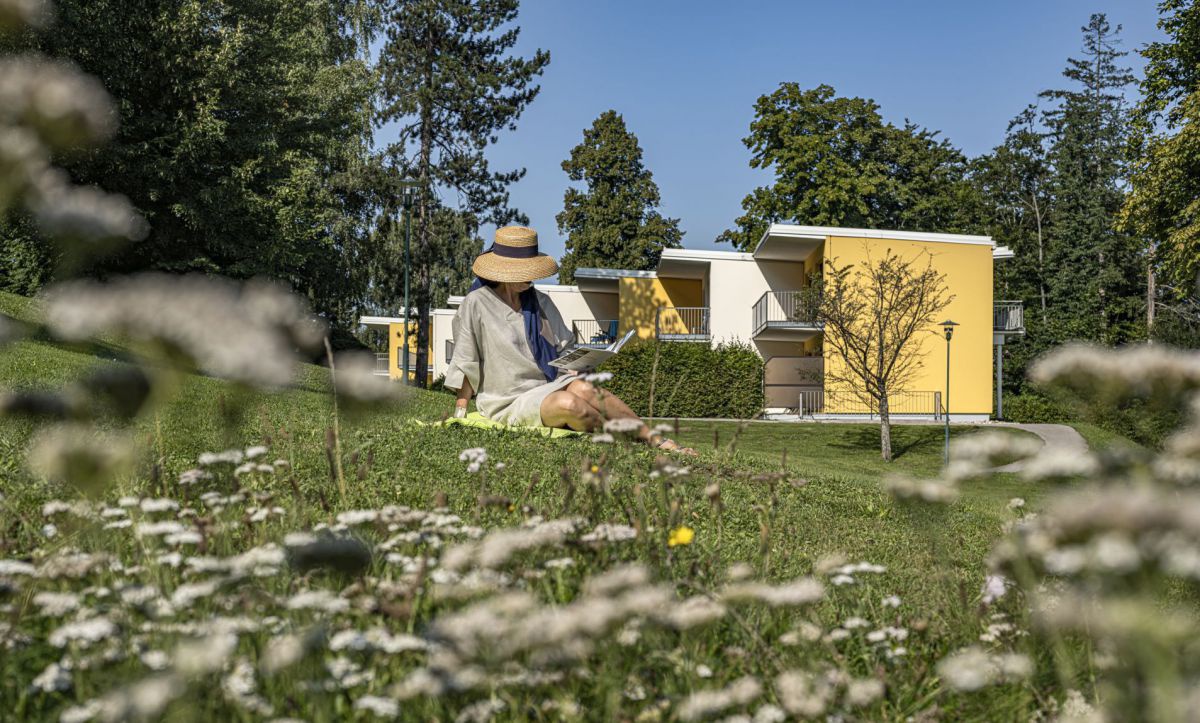 Frau mit Sonnenhut sitzt in der Wiese.
