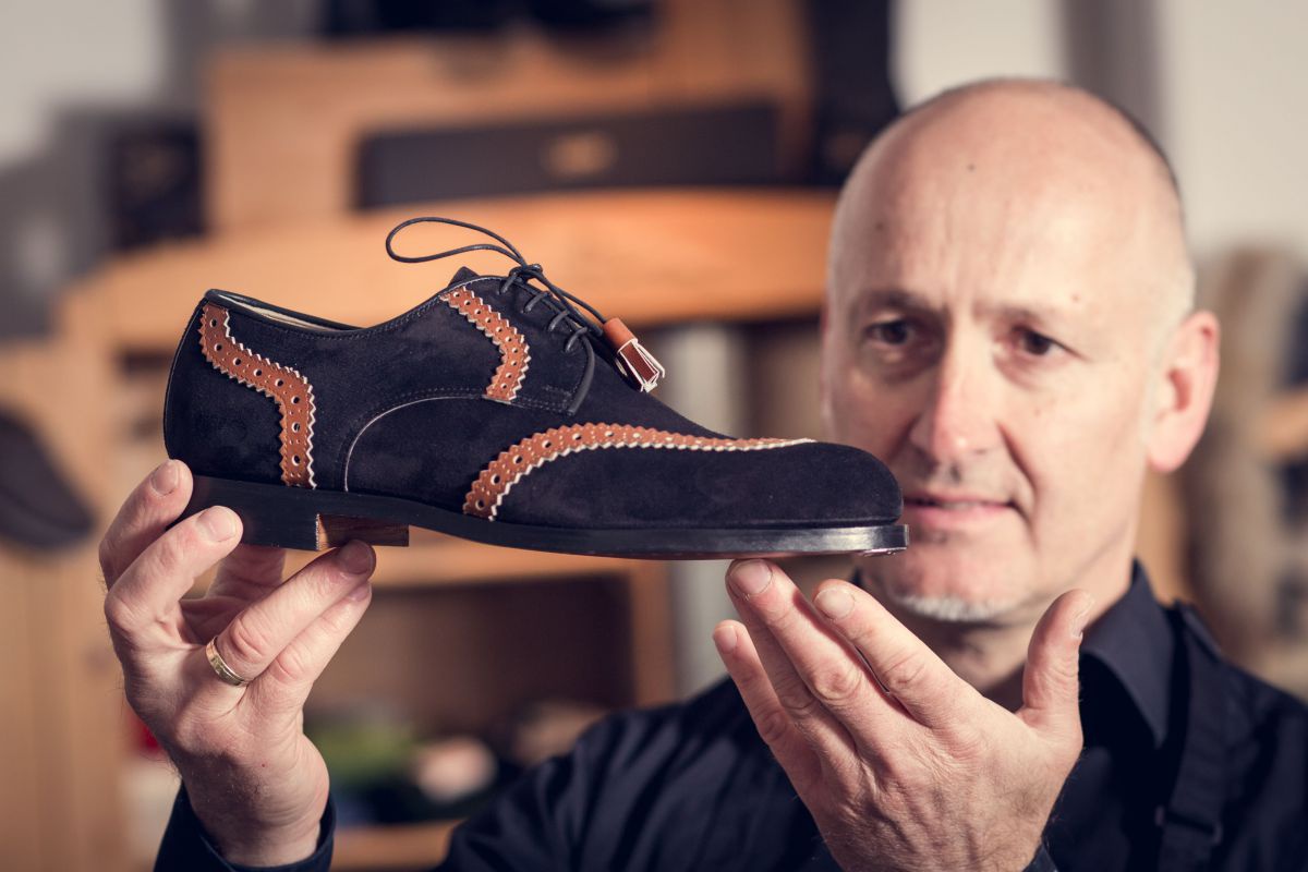 Ernst Knapp hält einen schwarzen Schuh mit braunen Dekorstreifen.