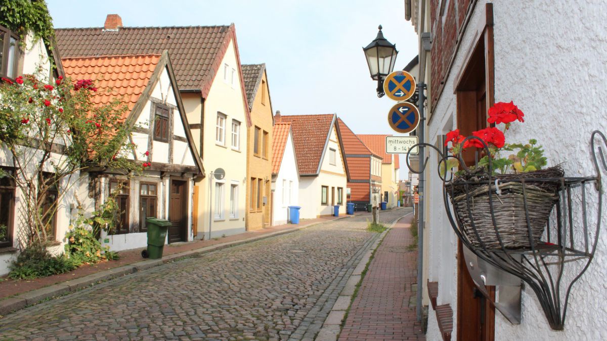 Schmale Gasse mit Kopfsteinpflaster, links und rechts herausgeputzte Häuschen.