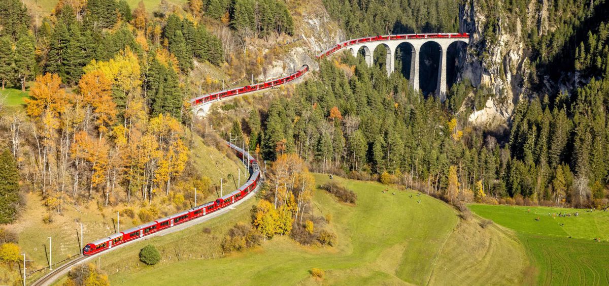 Roter Zug schlänhgelt sich über Viadukt dirch die Landschaft.
