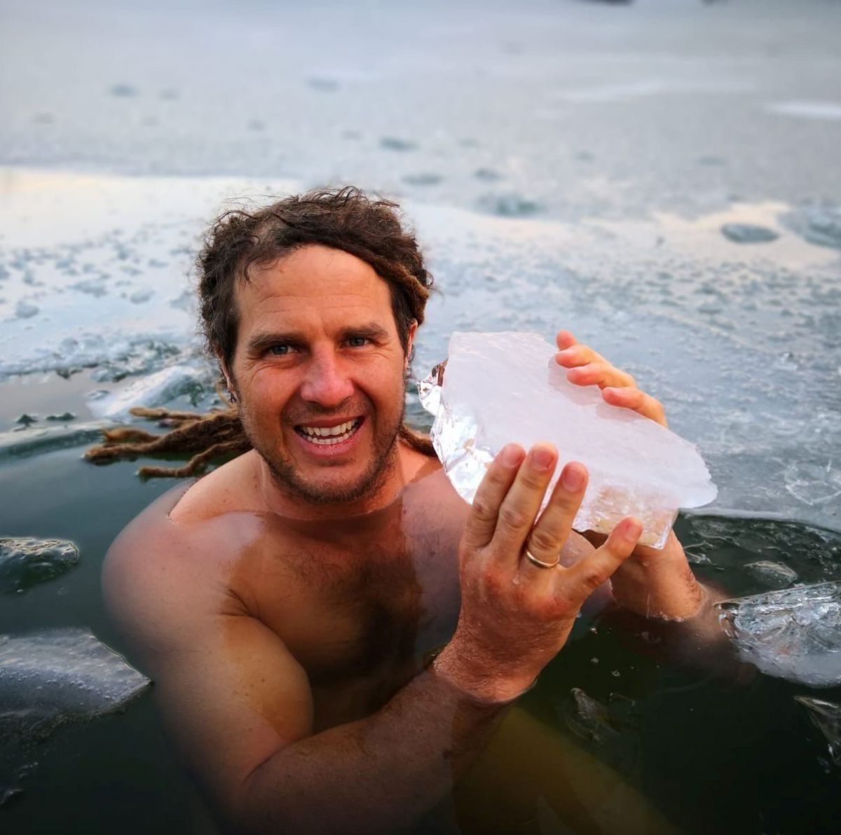 Daniel Fetz in einem Loch, dass er ins Eis gehackt hat. in den Händen hält er ein Stück Eis, ca. 5 cm dick.
