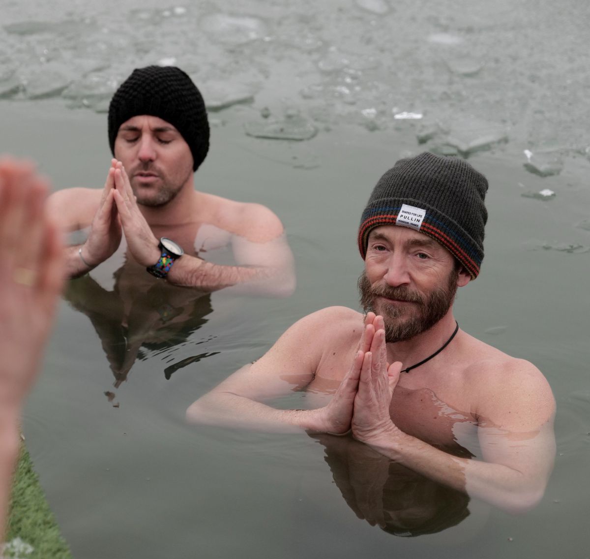 2 Männer stehem bis zum Hals im eisigen Wasser, die Hände vor dem Gesicht gefaltet.