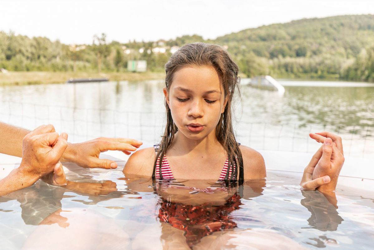 Mädchen im kalten Wasser, links und rechts Hände, die sie halten.
