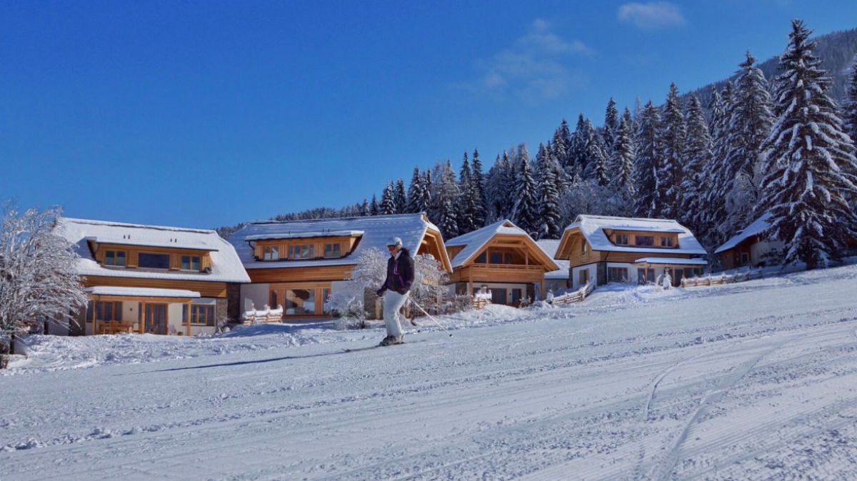 Chalets, daneben gleich die Piste mit einer Schiläuferin.