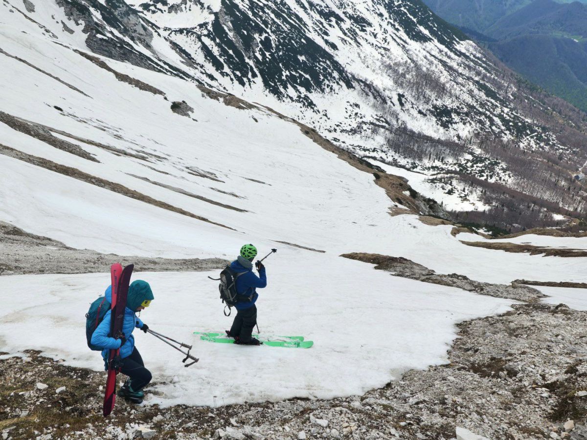Zwei Tourengeher beim Abstieg über einen von schroffen felsigen Abhang, der großteils schneebedeckt ist.