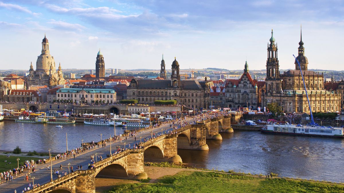Blick über die Augustbücke und die Elbe auf die Altstadt Dresdens mit mehreren historischen Gebäuden. Auf der Elbe liegen Schiffe im Hafen.
