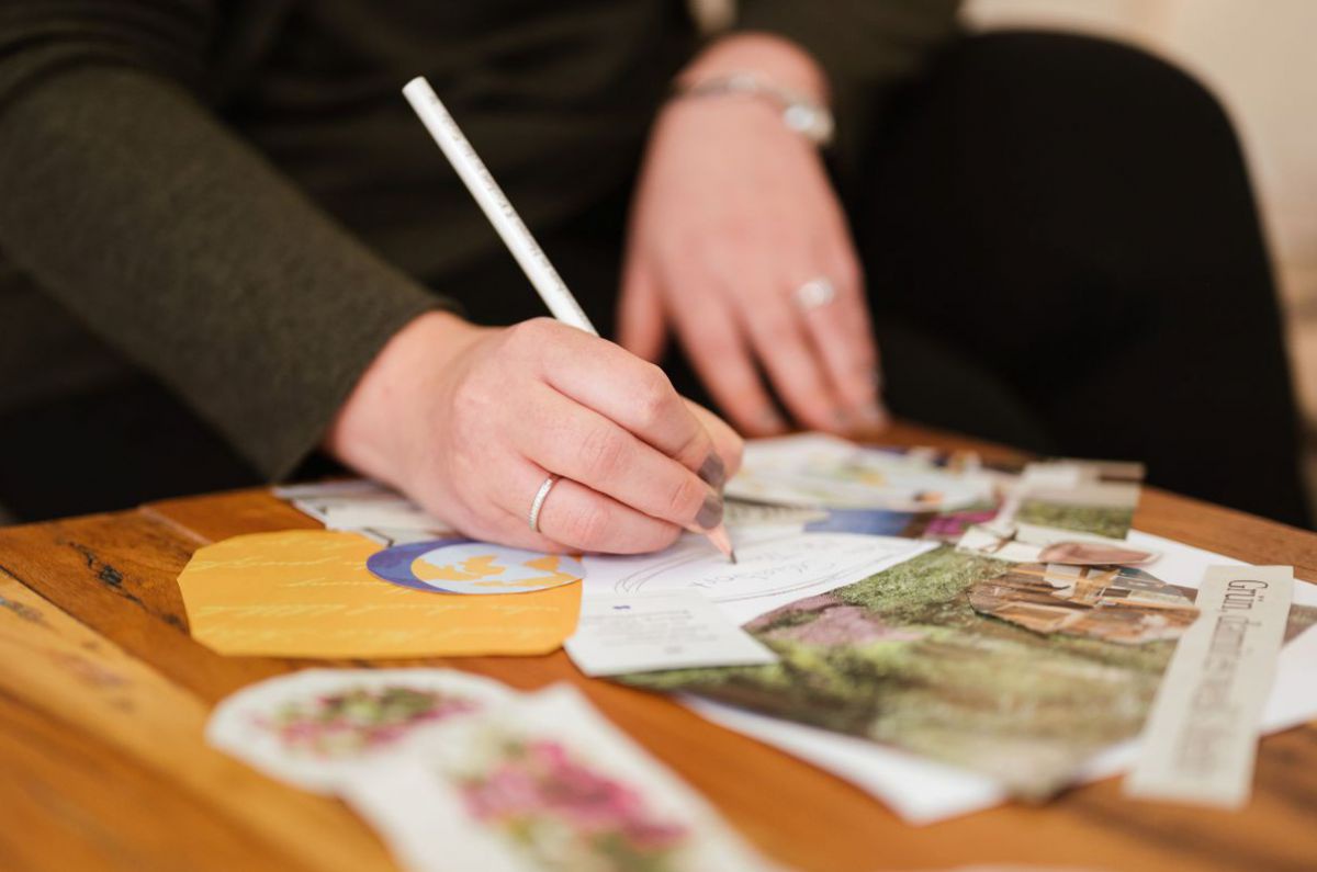 Eine Frau schreibt etwas mit Bleistift auf eine Collage aus Bildausschnitten und Notizpapier.