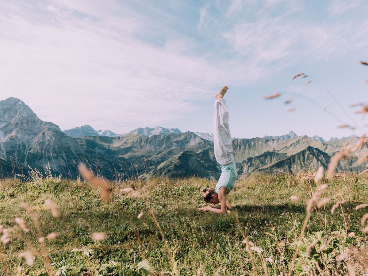 Eine Frau macht Yoga auf einer hochgelegenen Wiese in den Bergen.