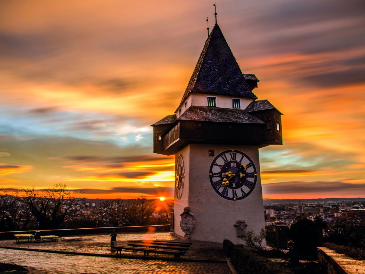 Der Uhrturm auf dem Schloßberg in Graz vor einem eindrucksvoll gefärbten Himmel bei Sonnenuntergang.