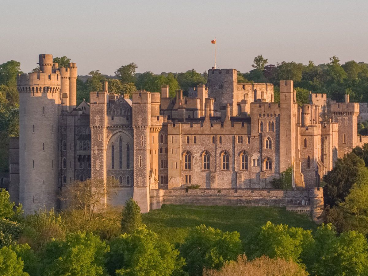 Die eindrucksvolle Schlossanlage von Arundel Castle: Steinmauern, Spitzbögen, Türme und Zinnen inmitten grüner Wiesen und Wälder.