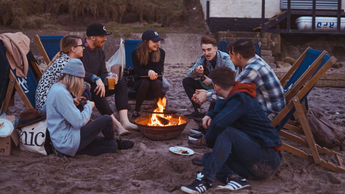 Eine Gruppe junger Leute picknicken am Strand und grillen an einem Lagerfeuer.