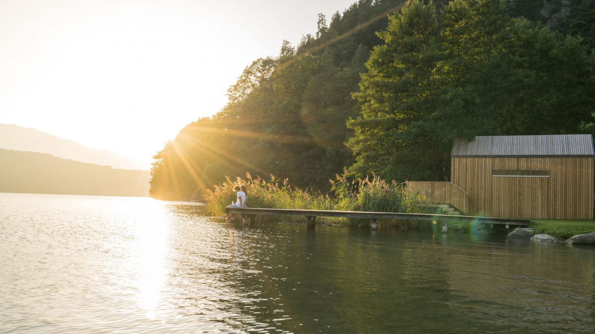 Paar sitzt bei Sonnenuntergang am Ende eines Steges am Millstättersee.