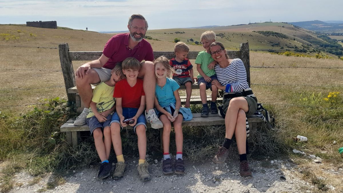 Familie Lobnig (2 Erwachsene und 5 Kinder) auf einer Bank mitten in der weiten Landschaft Südenglands.