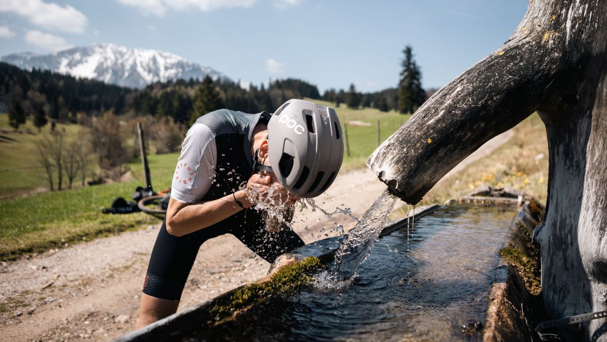 Radfahrer trinkt Wasser an einer Quelle.