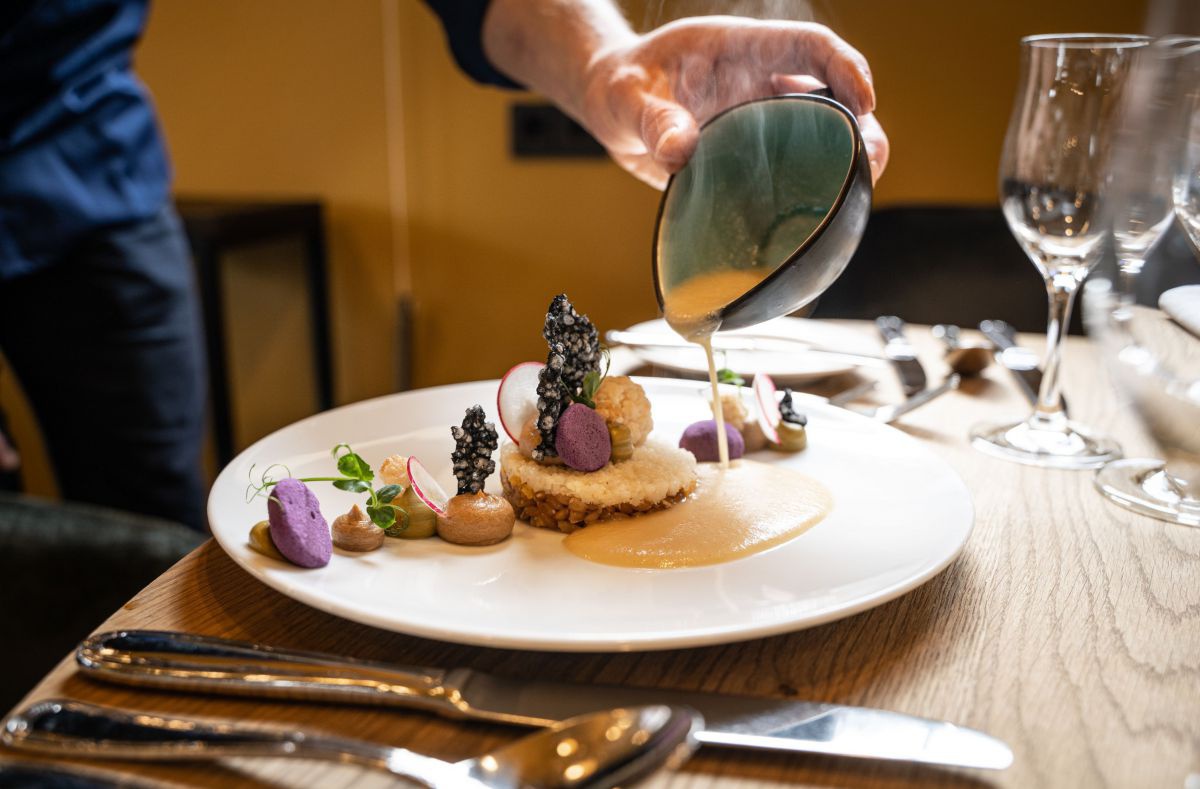 Koch leert eine Sauce über ein kunstvoll angerichtetes Gericht auf den Teller.