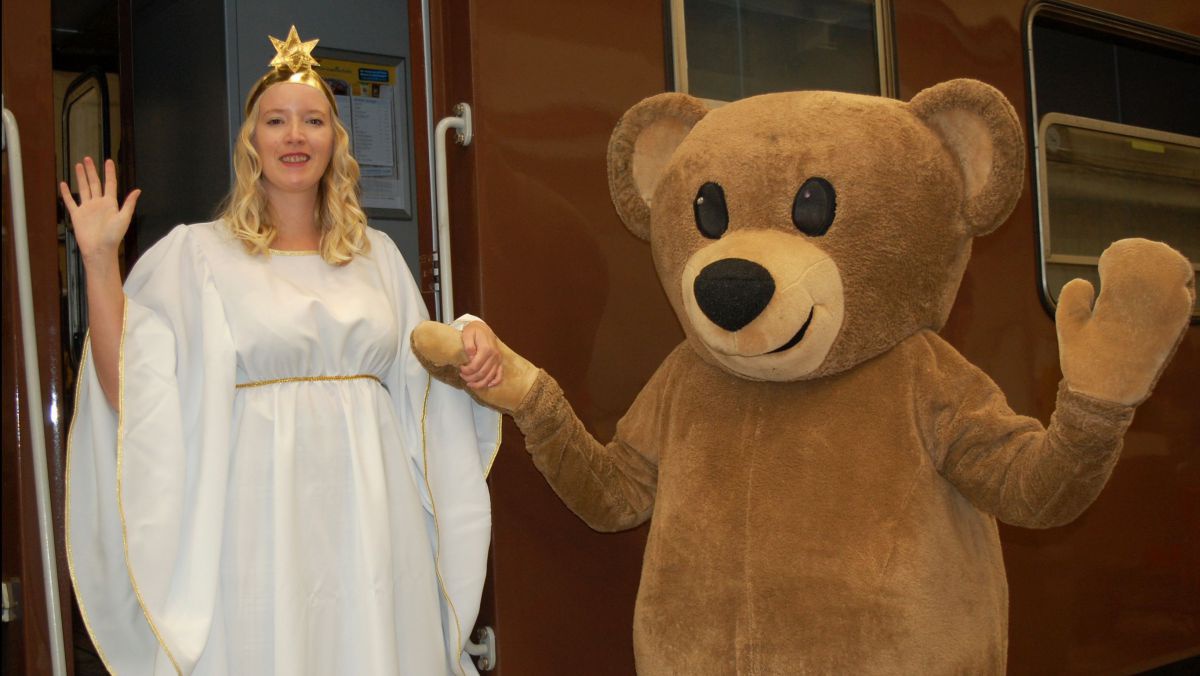 Frau als Christkind verkleidet und eine als Bär verkleidete Person vor einem Waggon.