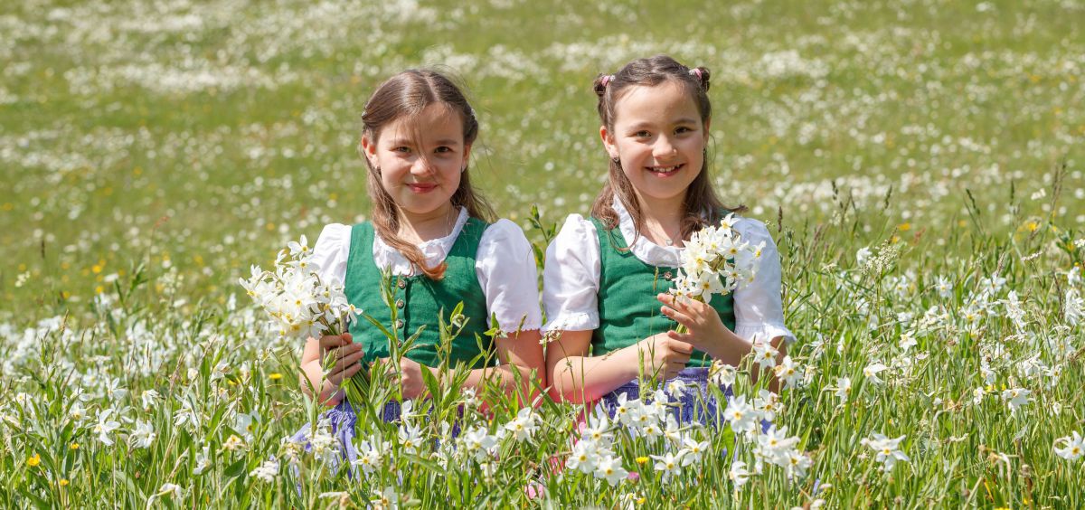 2 Mädchen in Tracht in einem Narzisenfeld.