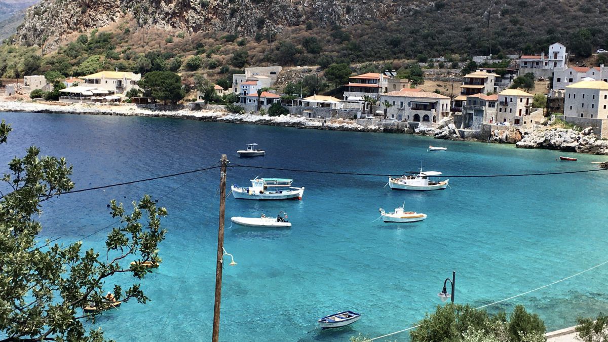 Boote schweben scheinbar auf der klaren türkisblauen Wasserfläche einer Bucht auf der griechischen Halbinsel Mani.