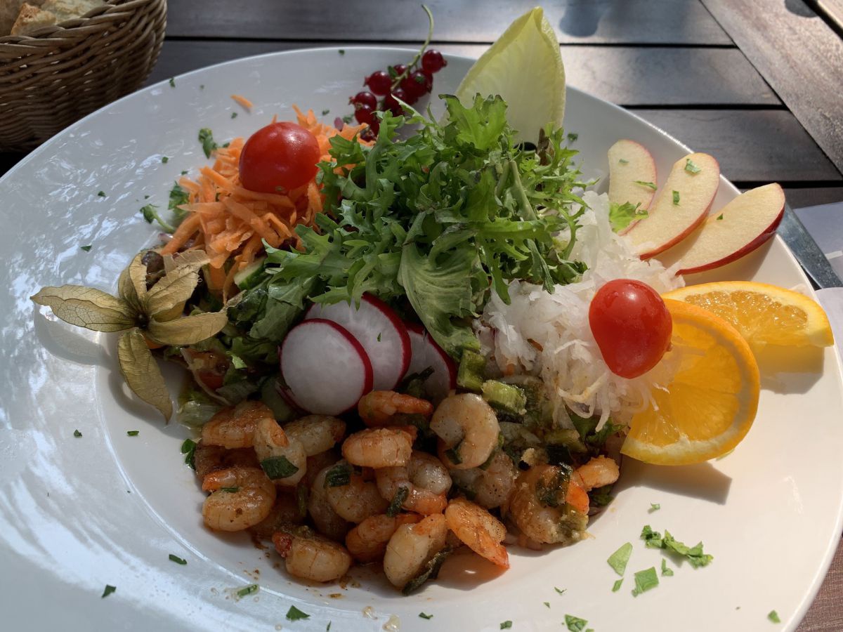 Schrimps mit buntem Salat und Zitronenscheiben auf einem weißen Teller angerichtet.