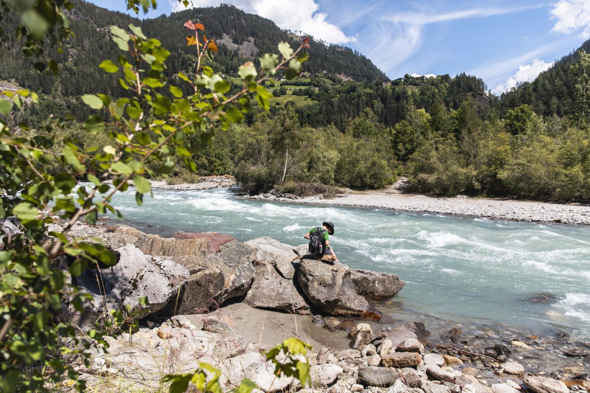 Ein Wanderer ruht sich auf einem Felsen am Ufer der Isel aus.