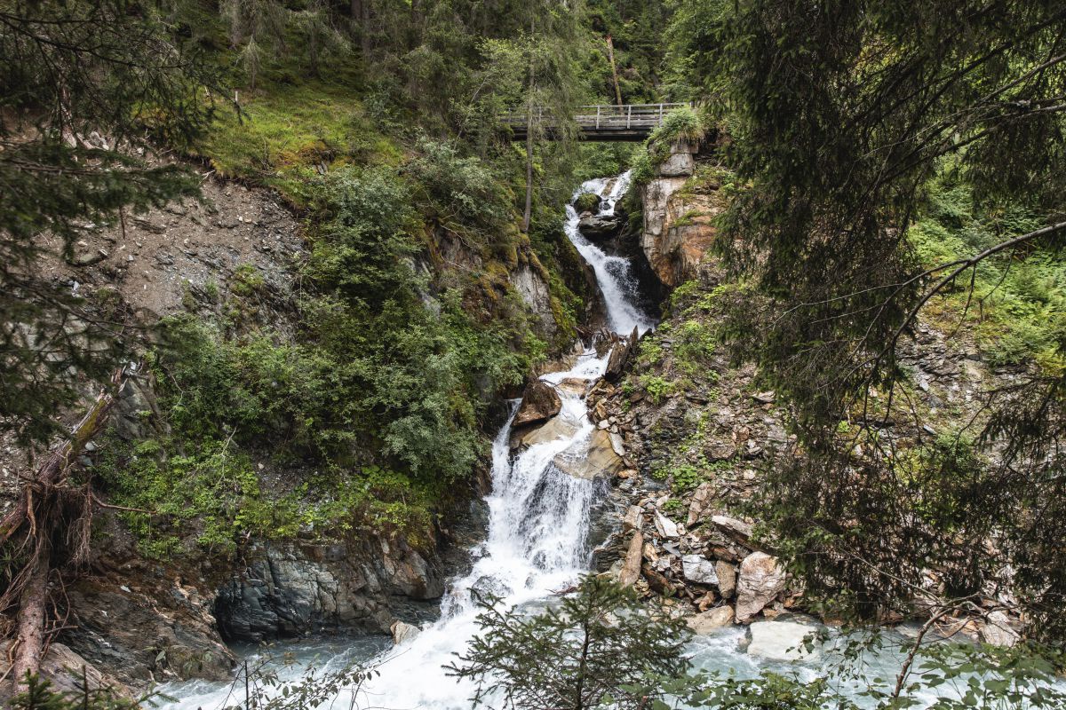 Wasserfall im Wald: der Wanderweg führt über eine Holzbrücke über den Fluss Isel, der sich hier die Felsen hinunter stürzt.
