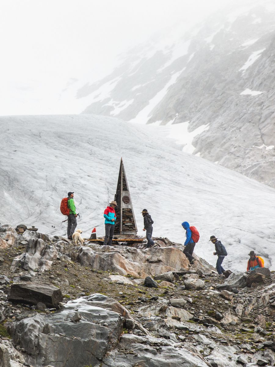 6 Wanderer treffen inmitten karger Felslandschaft im Gebirge auf eine Pyramide aus Stahl.