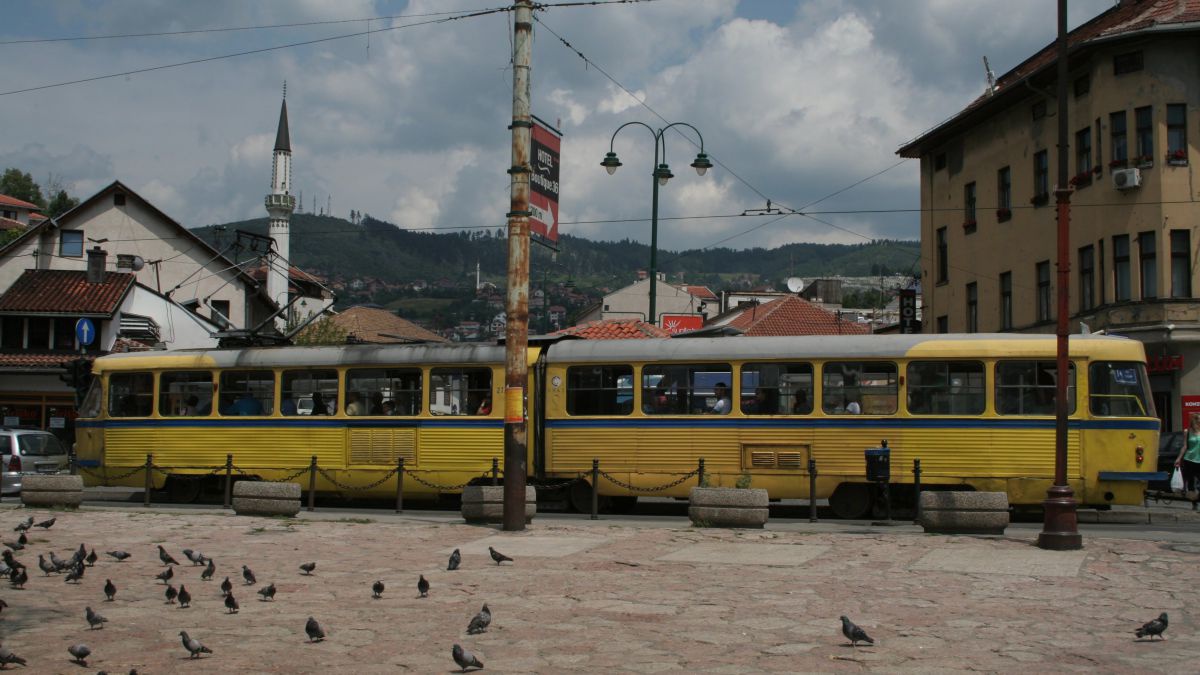 In die Jahre gekommene gelbe Straßenbahn auf einem Platz der von Tauben bevölkert ist.