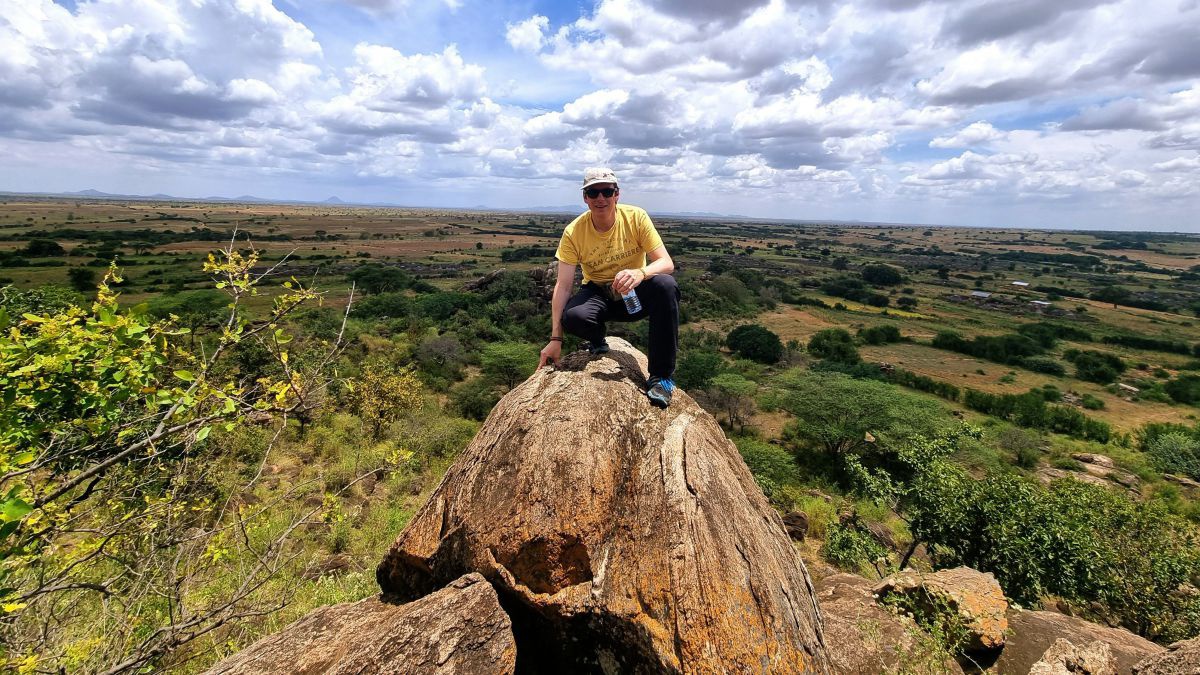 Mann sitzt auf einem Stein, dahinter eine weite Ebene eines Nationalparks.