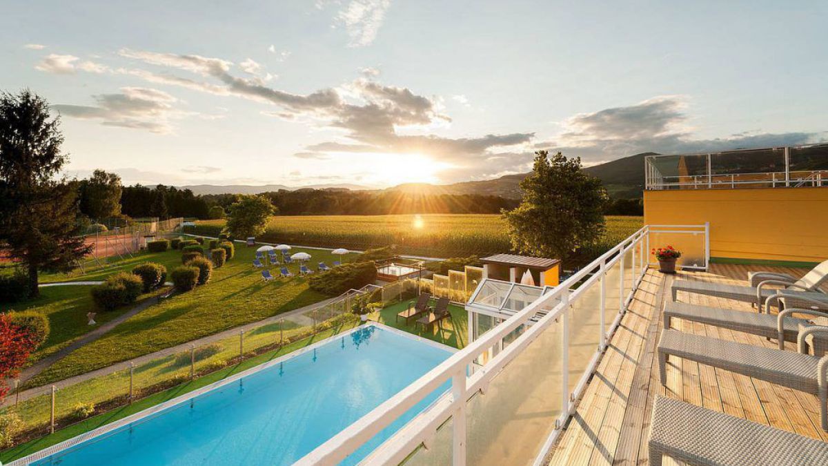 Blick von der Hotelterasse Hotel über einen Pool in die untergehende Sonne.