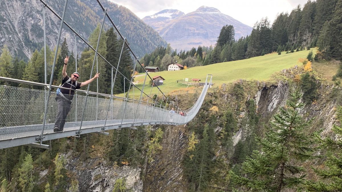 Gruppe überquert auf einer Hängebrücke aus Stahl eine Schlucht. Ferdinand Kaineder blickt zur Kamera und macht mit beiden Händen das Victory-Zeichen.