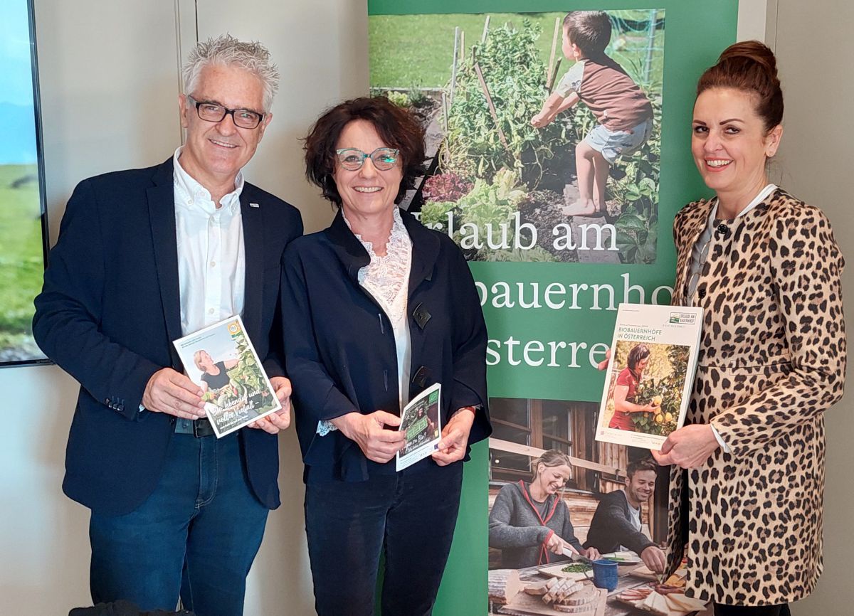 Hans Embacher, Susanne Maier, Sandra Neukart stehen vor einem Urlaub am Bauernhof -Plakat und halten Broschüren in Händen.