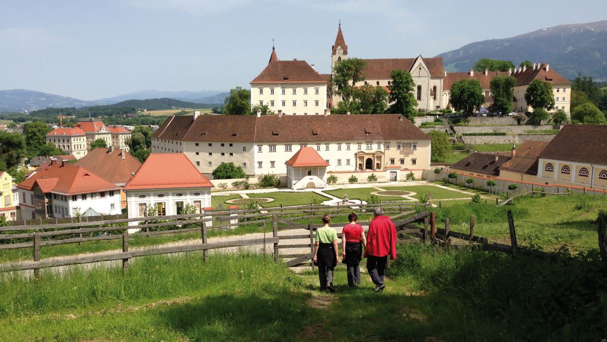 Drei Pilger wandern auf einem Wiesenweg in Richtung Stift St. Paul im Lavanttal.