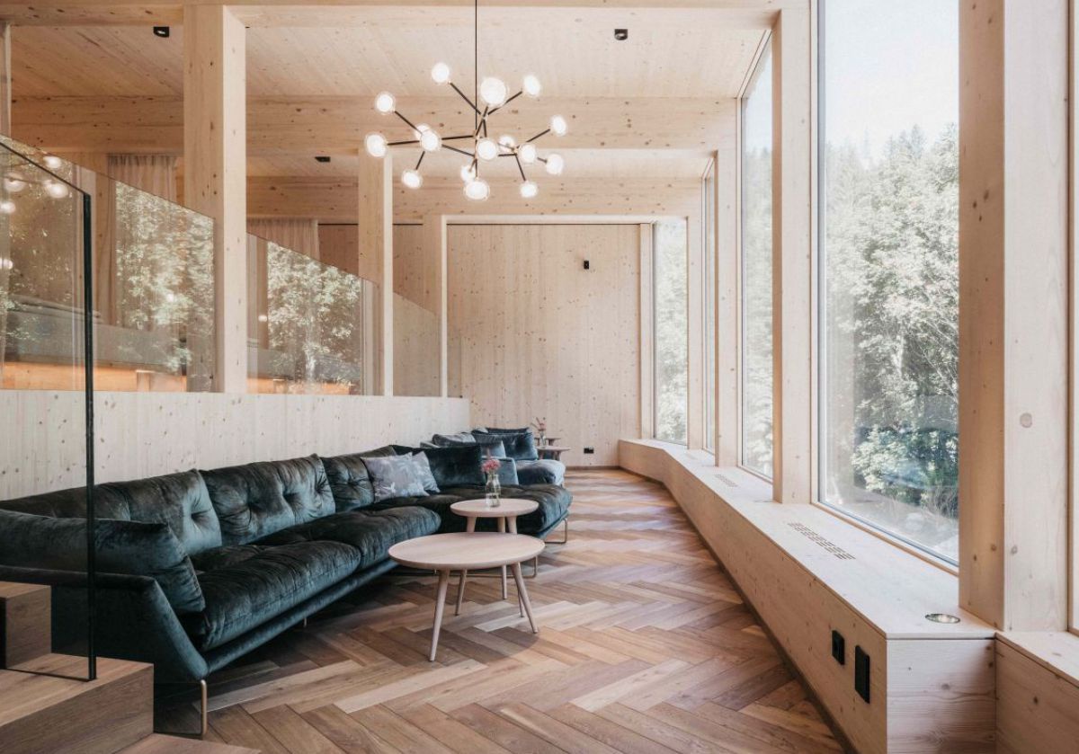 Raum mit Glaswand nach außen, viel Holz, schwarze Ledergarntur und runde Holztische.