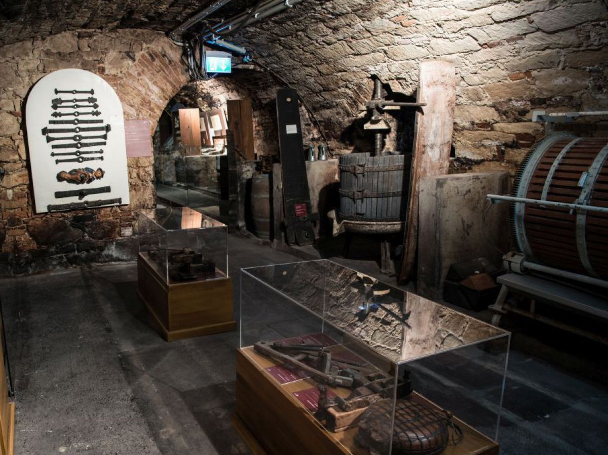 In einem alten gemauerten Kellergewölbe sind Gläserne Schaukästen angeordnet, in denen historische Utensilien zur Weinherstellung ausgestellt sind. Man sieht auch eine alte Presse und Fässer. An der Mauer hängen weitere Ausstellungsstücke.