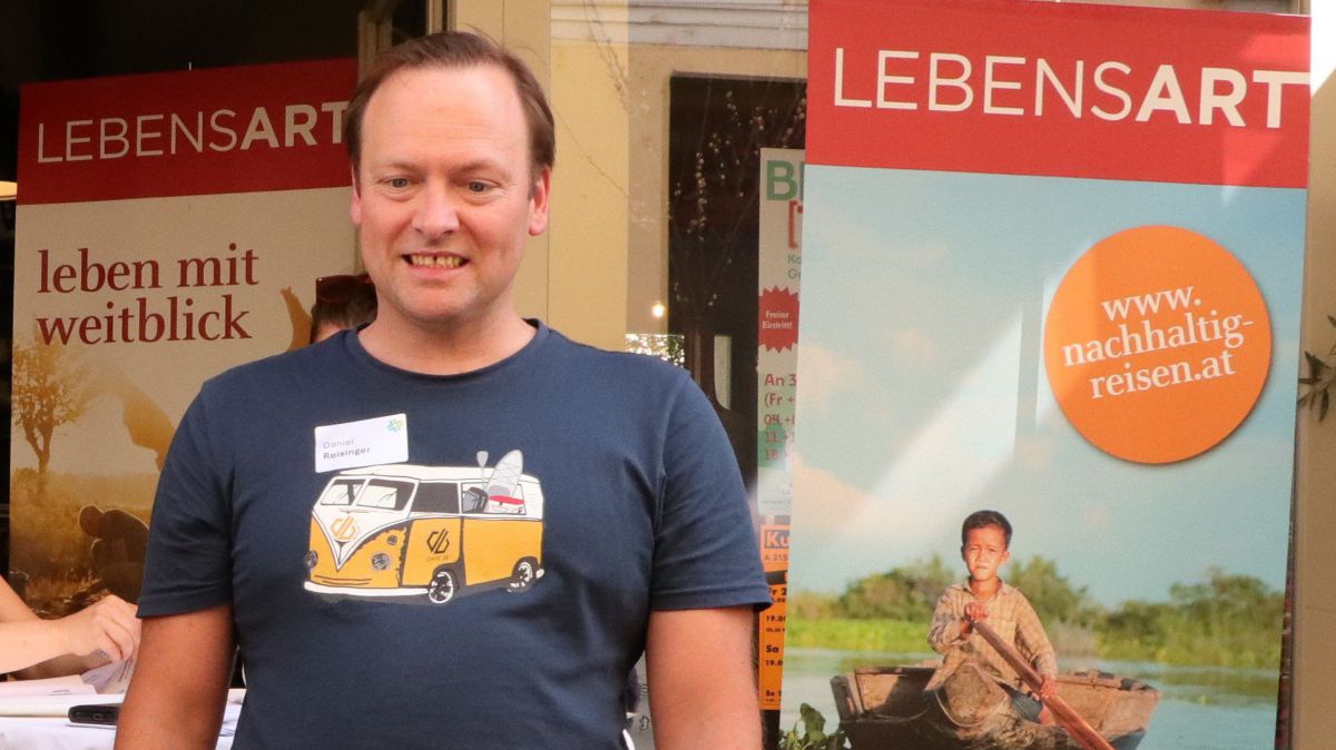 Mann mit Autobus am Leiberl vor dem Lebensart-reisen Transparent.