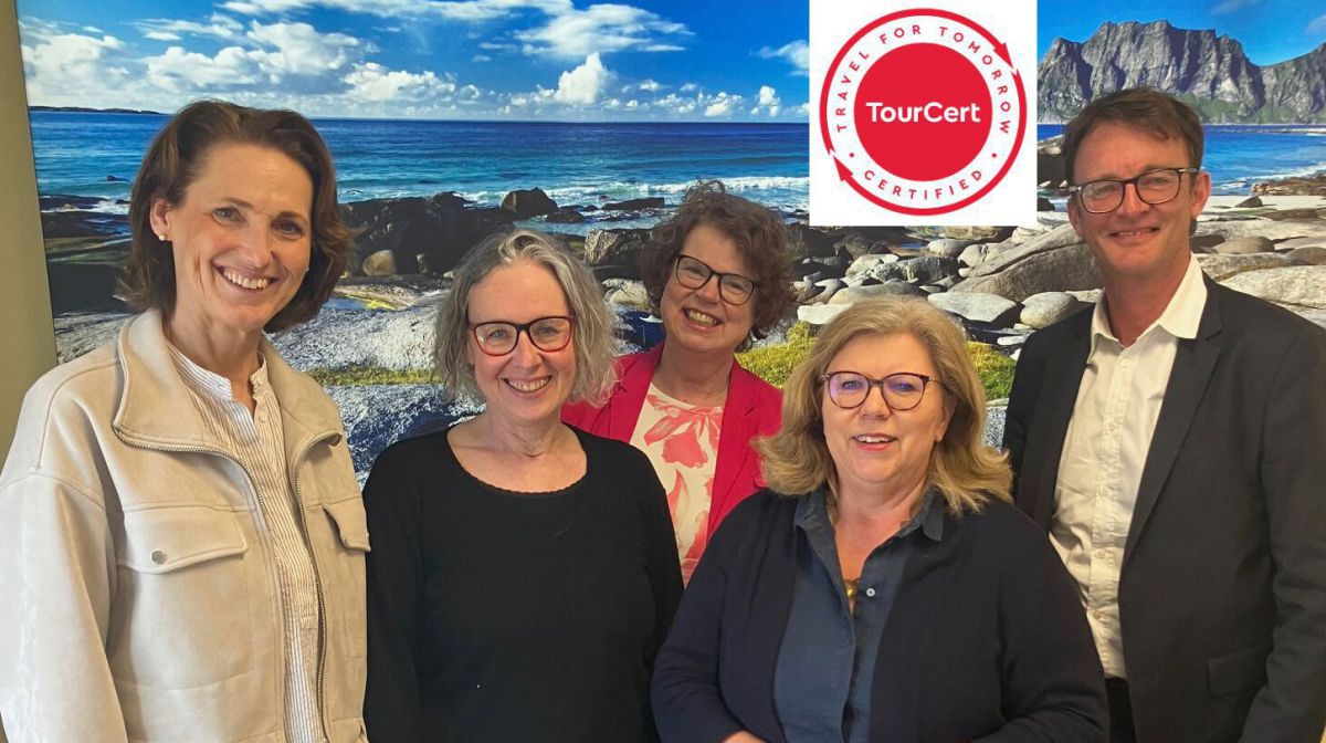 5 Personen vor einem Bild mit Küstenlandschaft und Tourcert-Logo.
