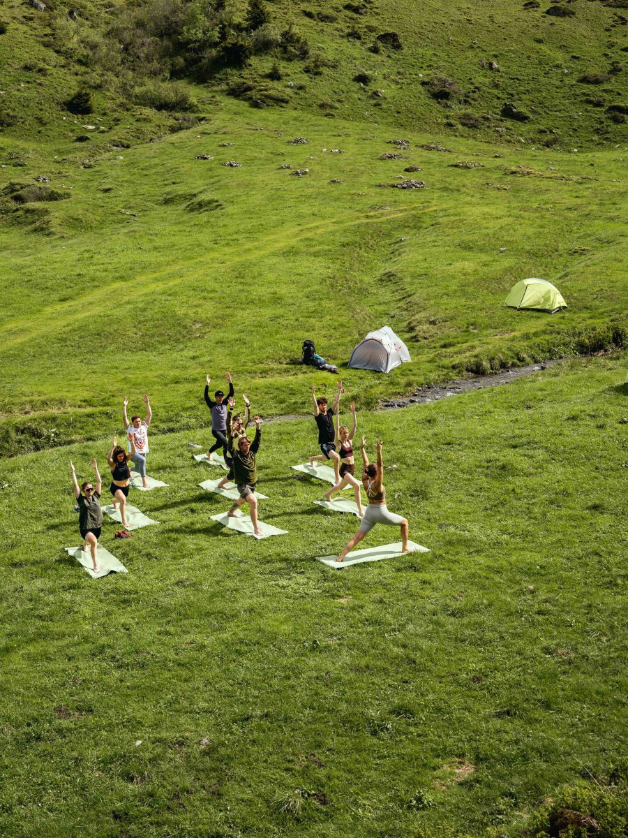 Gruppe beim Yoga auf einer Almwiese. Im Hintergrund Zelte.