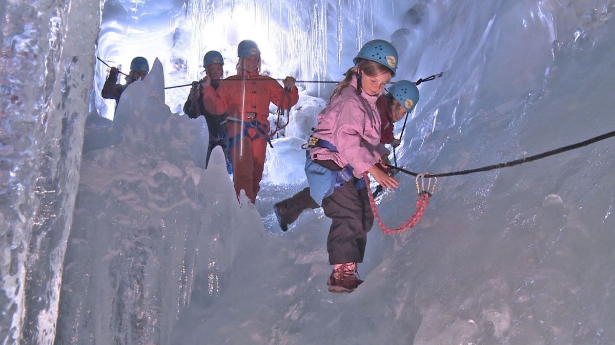 Mehrere Personen und Kinder mit Helmen und Kletterausrüstung auf dem gesicherten Weg durch die Eishöhle.
