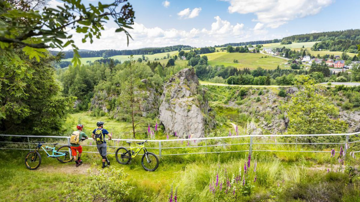 Zwei Radfahrer und ihre Räder machen eine Pause und genießen an einen Weidezaun gelehnt die Landschaft im Erzgebirge.