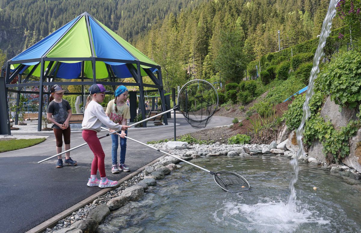 Zwei Kinder versuchen mit Keschernetzen kleine Bälle aus einem Wasserbecken zu fischen, in welches sprudelnd Wasser hineinfällt.