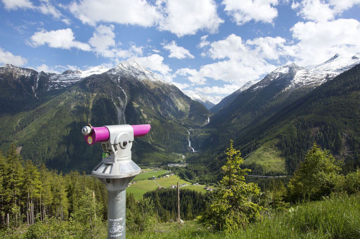 Blick von einem Aussichtspunkt auf ein Bergpanorama. In der linken Bildhälfte steht ein Münzfernrohr im Vordergrund.