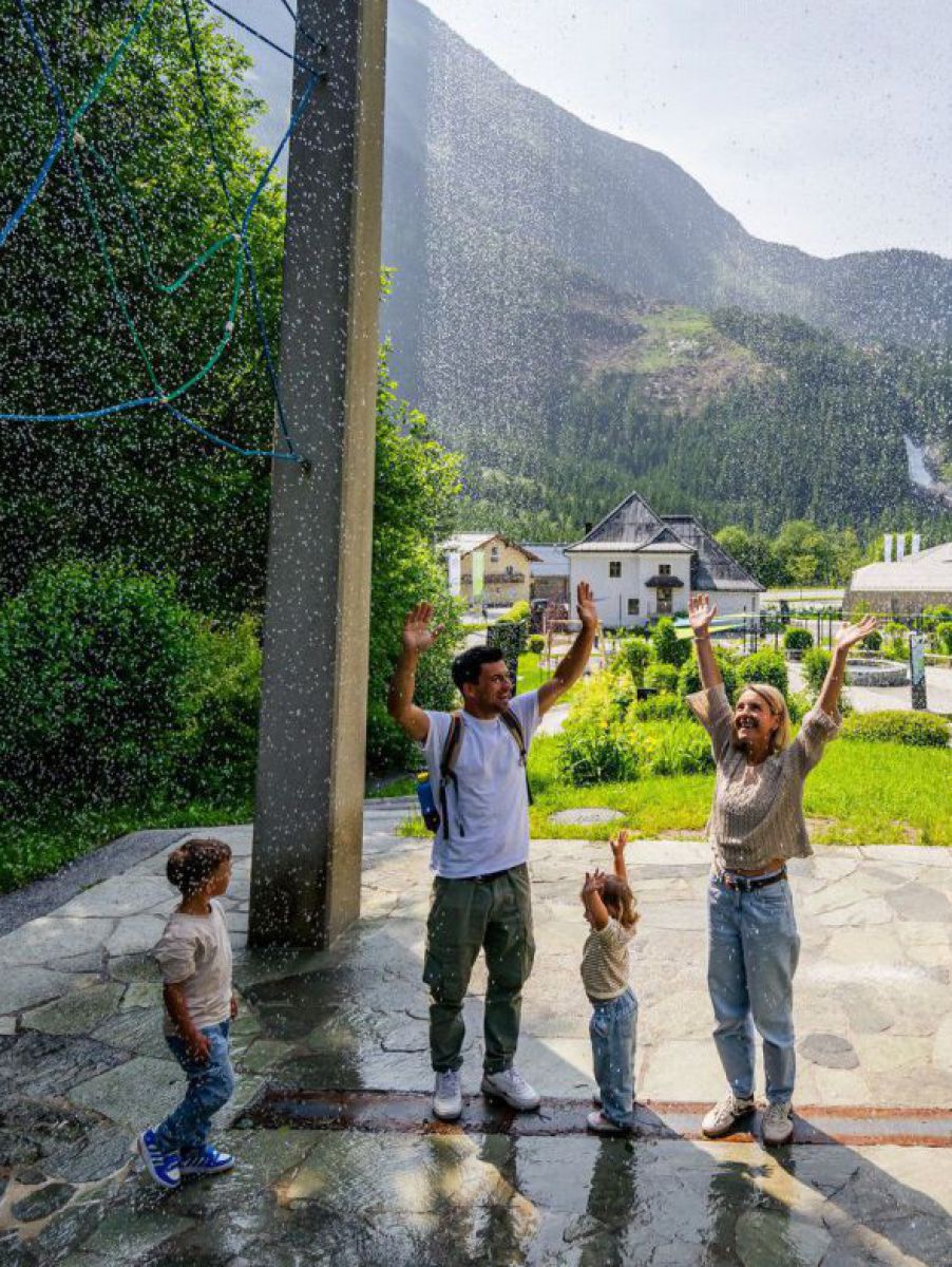 Ein Paar mit zwei Kleinkindern bei einer Station der Erlebniswelt Krimmler WasserWelten. Sie stehen mit erhobenen Armen zwischen Steinsäulen, von allen Seiten kommt Wasser als feiner Sprühnebel.