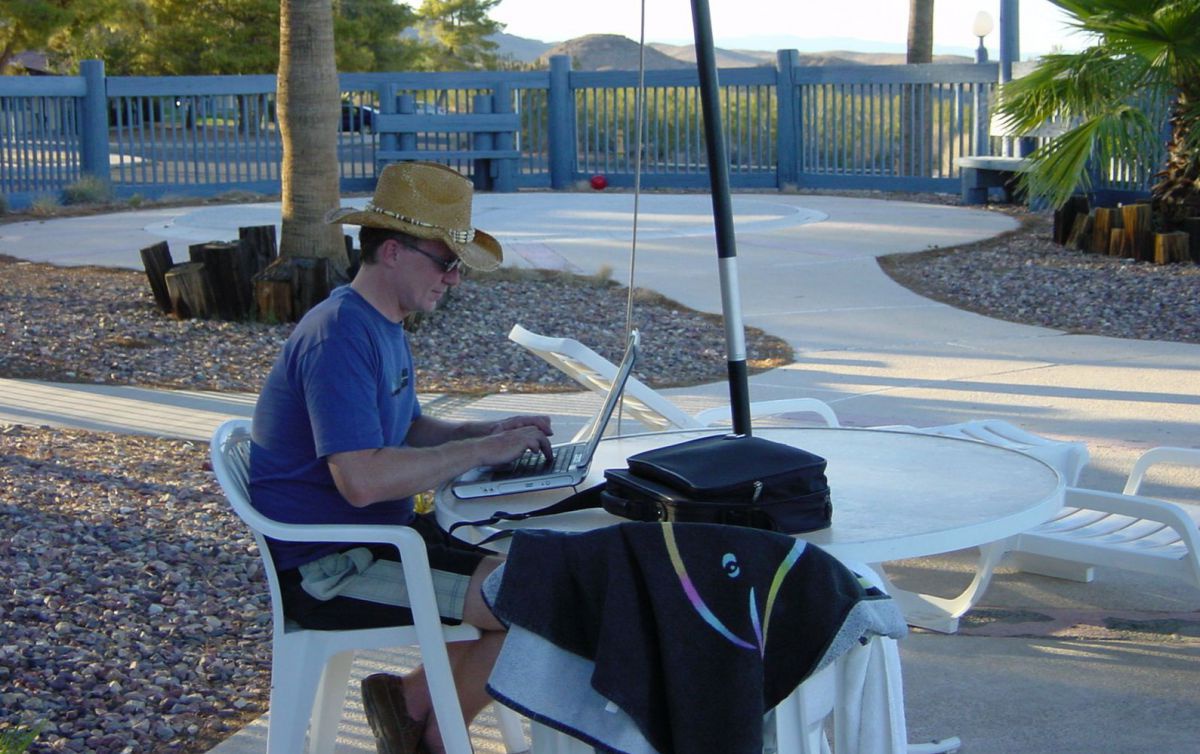 Christian Brandstätter sitzt mit seinem Laptop im Freien an einem Tisch.