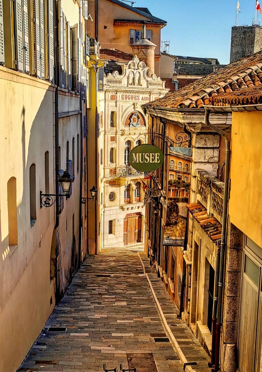 Blick in eine enge, steingepflasterte Gasse zwischen den kunstvollen Fassaden historischer Stadthäuser.