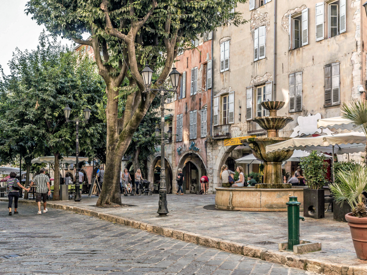 Der Platz ist mit groben Steinblöcken gepflastert, alte Bäume ud auch Palmen in Töpfen säumen die Gasse zwischen den historischen Arcadenhäusern. Ein alter Springbrunnen aus Stein steht im Zentrum.