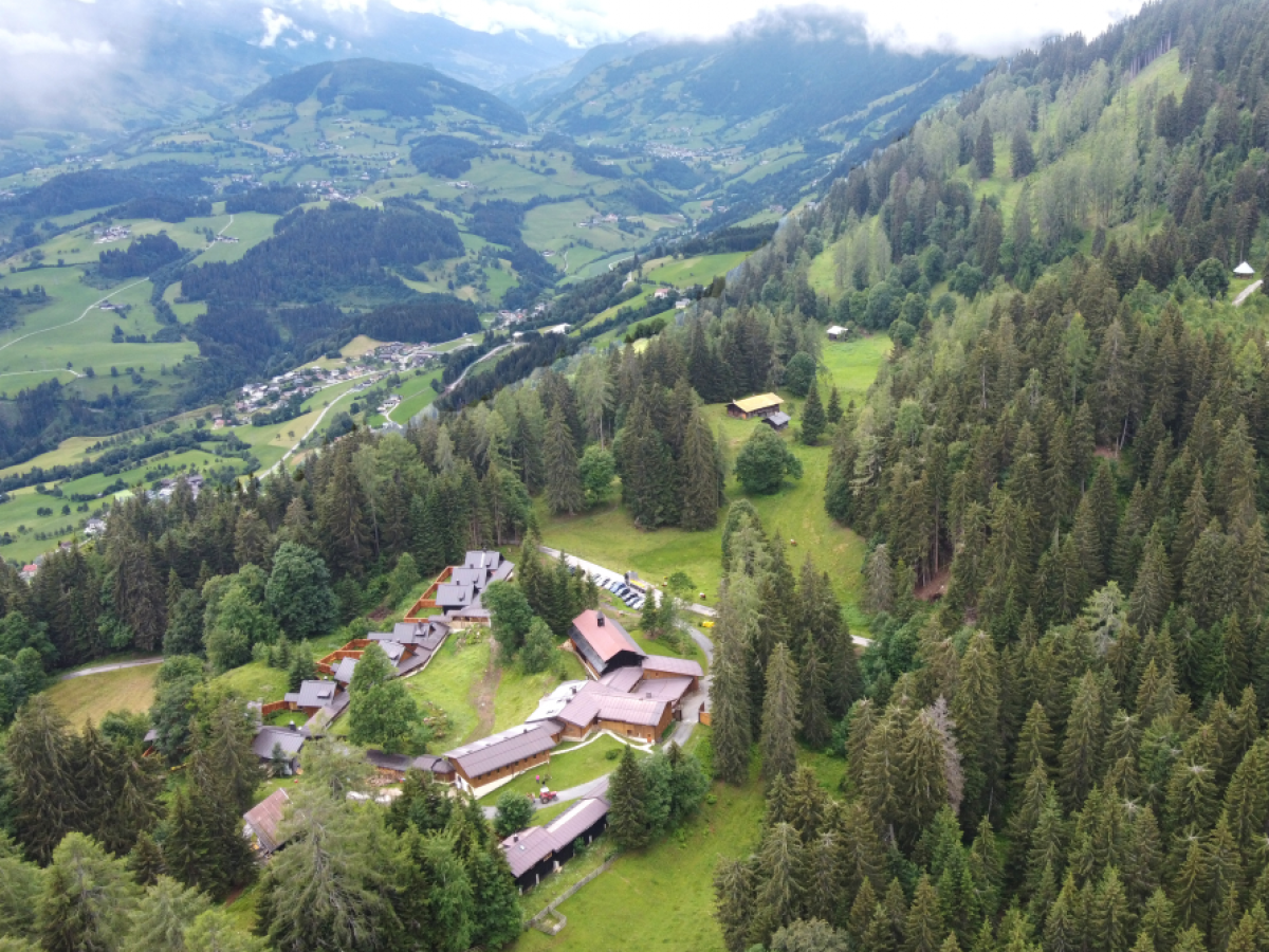 Luftaufnahme des Klosterareals in den Bergen, umgeben von grünen Wiesen und Nadelwäldern.